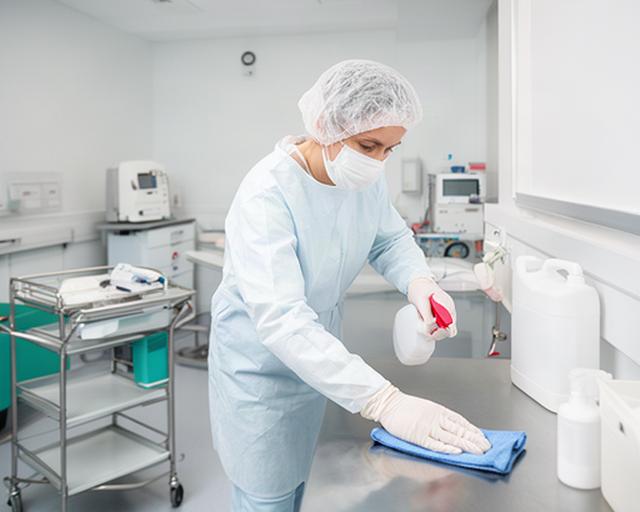 Hygienefachperson bei der Flächendesinfektion in einem modernen Klinikraum